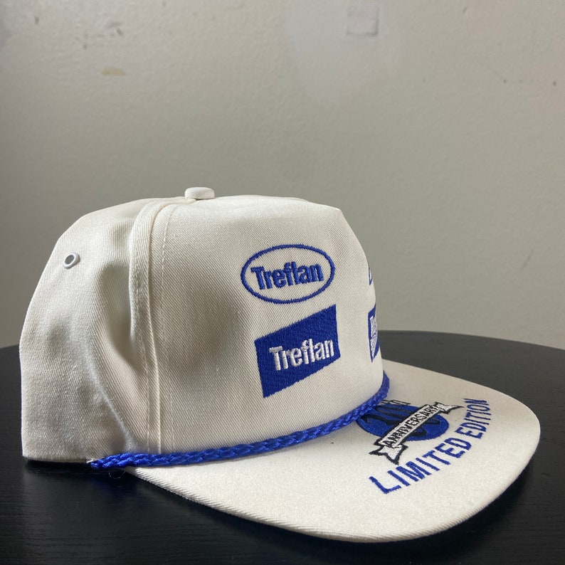 May include: White baseball cap with blue embroidered logos, including "Treflan" and "Anniversary Edition Limited Edition".