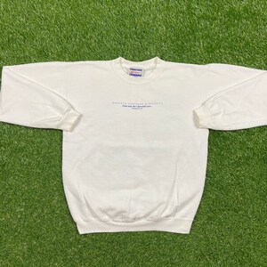 Könnte beinhalten: Ein weißes Langarm-Sweatshirt mit dem Text "KENNETH COPELAND MINISTRIES" und "Fear not, for I am with you..." in Blau. Es hat einen Rundhalsausschnitt und gerippte Bündchen.