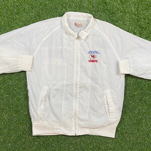 May include: White windbreaker jacket with a zipper closure and a Kansas City Chiefs logo on the left chest. The logo is embroidered in red, blue, and white and reads "Bank of  Dawn County  Golf  Classic  KC Chiefs".