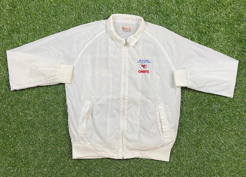 May include: White windbreaker jacket with a zipper closure and a Kansas City Chiefs logo on the left chest. The logo is embroidered in red, blue, and white and reads "Bank of  Dawn County  Golf  Classic  KC Chiefs".
