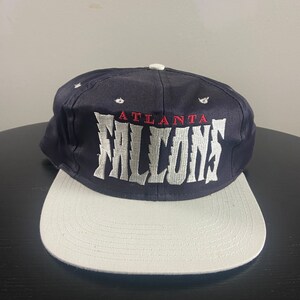 May include: A navy blue and white Atlanta Falcons baseball cap with the team name embroidered in white on the front.