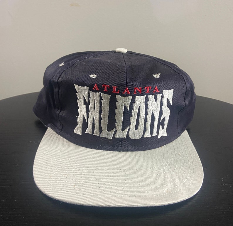 May include: A navy blue and white Atlanta Falcons baseball cap with the team name embroidered in white on the front.