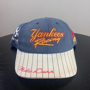 May include: A navy blue Yankees Racing baseball cap with a white and black striped brim. The cap features the text "Yankees Racing" in yellow and red script, and "Mike Dunn" in red script.