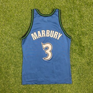 May include: Blue basketball jersey with the name "MARBURY" arched across the back and the number "3" in white. The jersey has green and black trim around the neck and armholes. The jersey is displayed on a green surface.