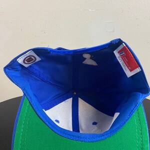 K&ouml;nnte beinhalten: Blaue und gr&uuml;ne Baseballkappe mit wei&szlig;em Innenfutter. Die Kappe hat ein Logo auf der Vorderseite und ein Etikett auf der Innenseite mit der Aufschrift "For the love of the game.  Officially licensed. Made in Thailand."