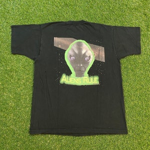 Może przedstawiać: Czarny T-shirt z zielonym nadrukiem kosmity i tekstem "Aliens Rule" nadrukowanym na plecach.
