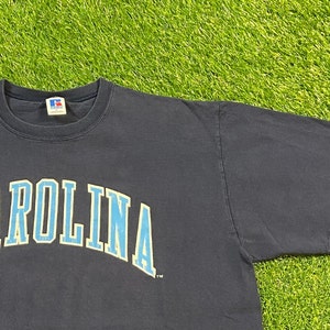 May include: A navy blue t-shirt with the word "CAROLINA" printed in light blue and yellow letters.