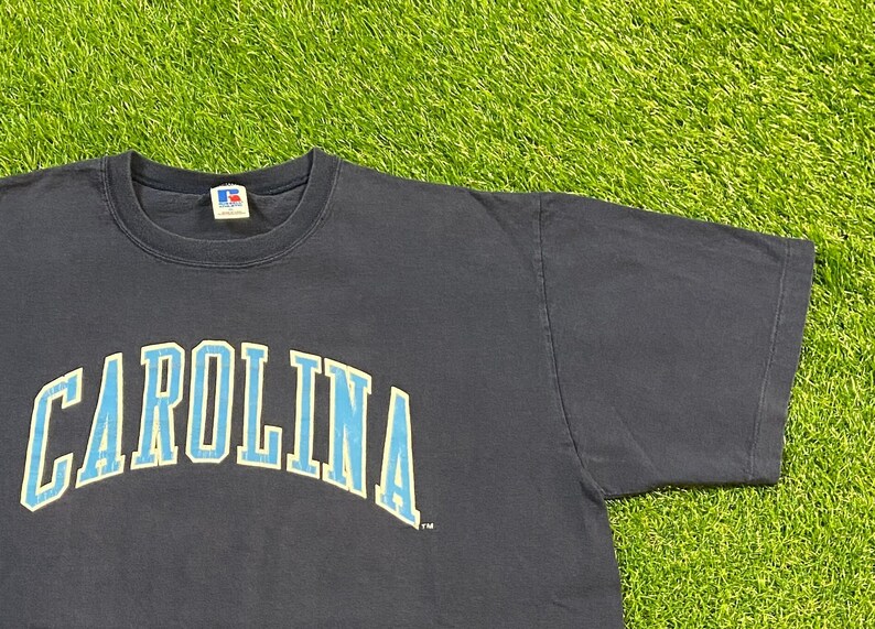 May include: A navy blue t-shirt with the word "CAROLINA" printed in light blue and yellow letters.