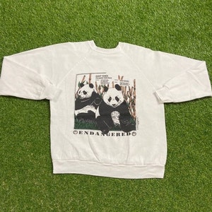 May include: White long-sleeve sweatshirt with a graphic of two giant pandas sitting on bamboo. The graphic includes the text "Giant Panda" and "Endangered".