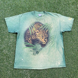 May include: Green t-shirt with a faded, tie-dye effect featuring a graphic print of a leopard in a jungle setting.