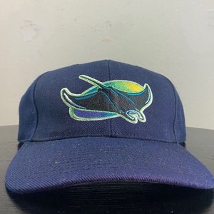 May include: Navy blue baseball cap featuring an embroidered logo of a manta ray in black, green, and purple. The cap has a curved brim and a structured crown. A stylish accessory for sports fans.