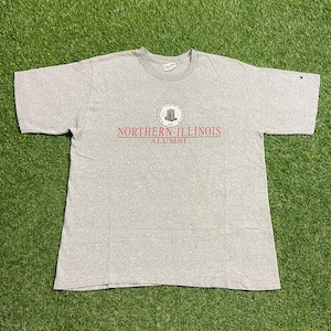 May include: A grey t-shirt with the words "NORTHERN ILLINOIS ALUMNI" in red and black. The shirt has a crew neck and short sleeves. A circular emblem is above the text.