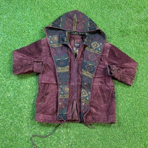 May include: A burgundy suede jacket with a patterned hood lining. The lining features a geometric design in shades of brown, green, and yellow. The jacket has a zipper closure and two pockets.