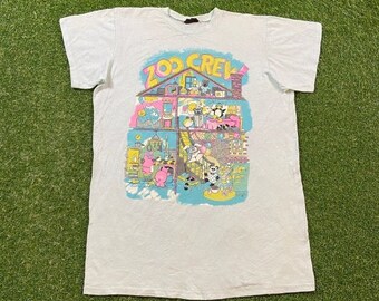 May include: White t-shirt with a cartoon graphic of a house with animals. The text "Zoo Crew" is printed on the house.