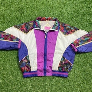 May include: A purple, white, and blue windbreaker jacket with a colorful abstract print. The jacket has a zipper closure and a stand-up collar.