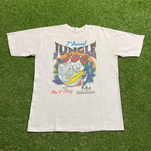 May include: White t-shirt featuring a colorful graphic for the "7th Annual Jungle Jog" event. The design includes a cartoon hippo wearing a yellow sash, palm trees, and the text "May 9th 1998 SANDYPINES".