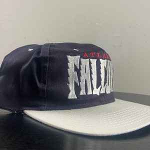 May include: A black and grey baseball cap with the text "ATLANTA FALCONS" embroidered in white on the front.