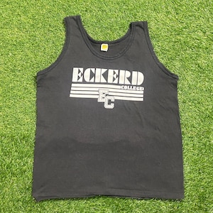 Puede incluir: Camiseta sin mangas negra con el texto "ECKERD COLLEGE" en letras blancas. La camiseta sin mangas tiene un estilo atlético clásico con cuello redondo y diseño sin mangas. La camiseta está hecha de un material suave y cómodo.