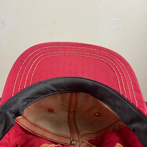 Op de afbeelding: Rode baseballpet met een zwarte rand en een beige mesh voering. De pet heeft een enkel stikseldetail rond de rand.