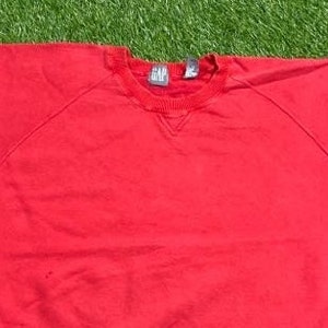 Pu&ograve; includere: Felpa rossa con collo rotondo e la scritta "GAP" sull'etichetta.