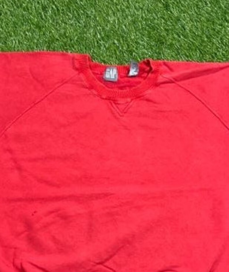 Pu&ograve; includere: Felpa rossa con collo rotondo e la scritta "GAP" sull'etichetta.
