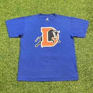 May include: A blue t-shirt featuring a large orange letter "D" with a black bull graphic. The shirt has short sleeves and a crew neck. The brand logo is visible on the upper chest.