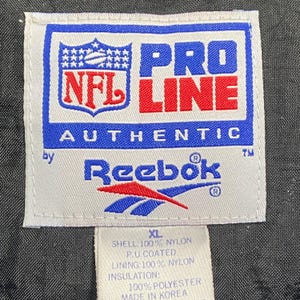Peut inclure: Une &eacute;tiquette blanche avec du texte bleu et rouge, avec le logo NFL et la marque "PRO LINE AUTHENTIC". Le logo Reebok est &eacute;galement visible. L'&eacute;tiquette indique que la veste est XL, en nylon et polyester.