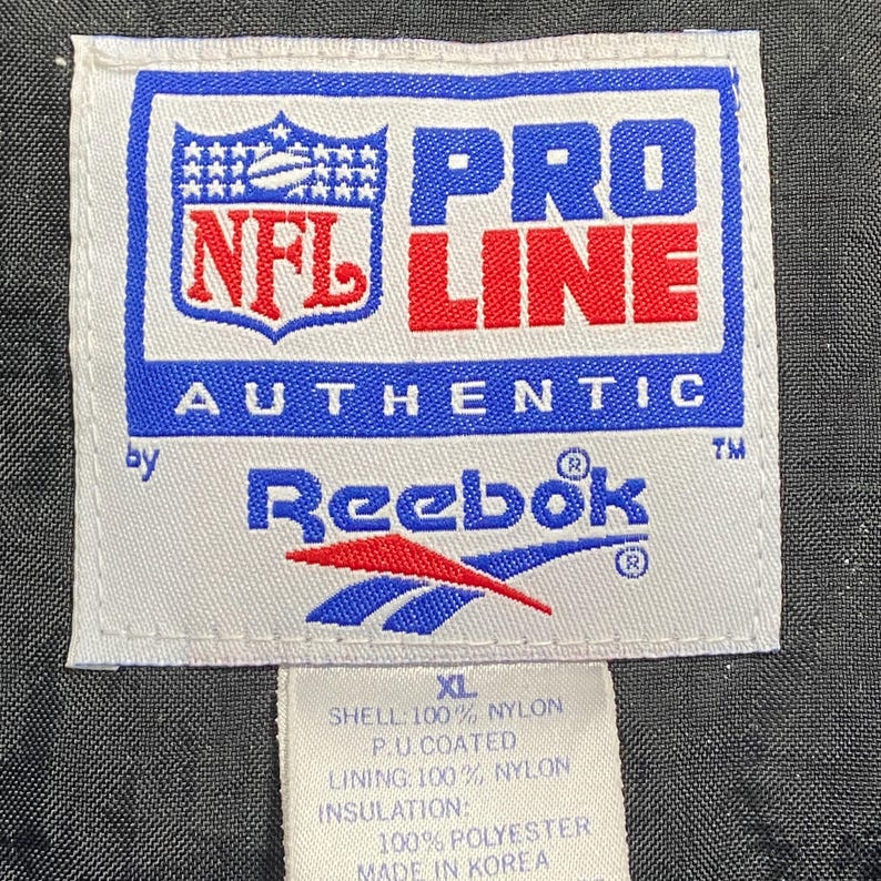 Peut inclure: Une &eacute;tiquette blanche avec du texte bleu et rouge, avec le logo NFL et la marque "PRO LINE AUTHENTIC". Le logo Reebok est &eacute;galement visible. L'&eacute;tiquette indique que la veste est XL, en nylon et polyester.