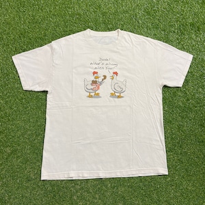 Könnte beinhalten: Weißes T-Shirt mit einer Cartoon-Illustration von zwei Hühnern. Ein Huhn hält einen Eimer mit Brathähnchen, das andere scheint überrascht. Der Text über den Hühnern lautet: "Dude! What's wrong with You!"