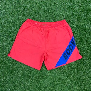 May include: Red swim trunks with a blue diagonal stripe and the word "BODY" in black letters.