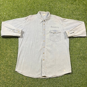 May include: Light blue denim shirt with long sleeves and a button-down front. The shirt features a chest pocket and the word "doors" embroidered in black. The shirt is laid flat on a green surface.