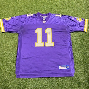 May include: Purple football jersey with the number 11 in yellow. The jersey has yellow accents on the sleeves and collar. The jersey is made of a mesh material and has a tag on the lower front.