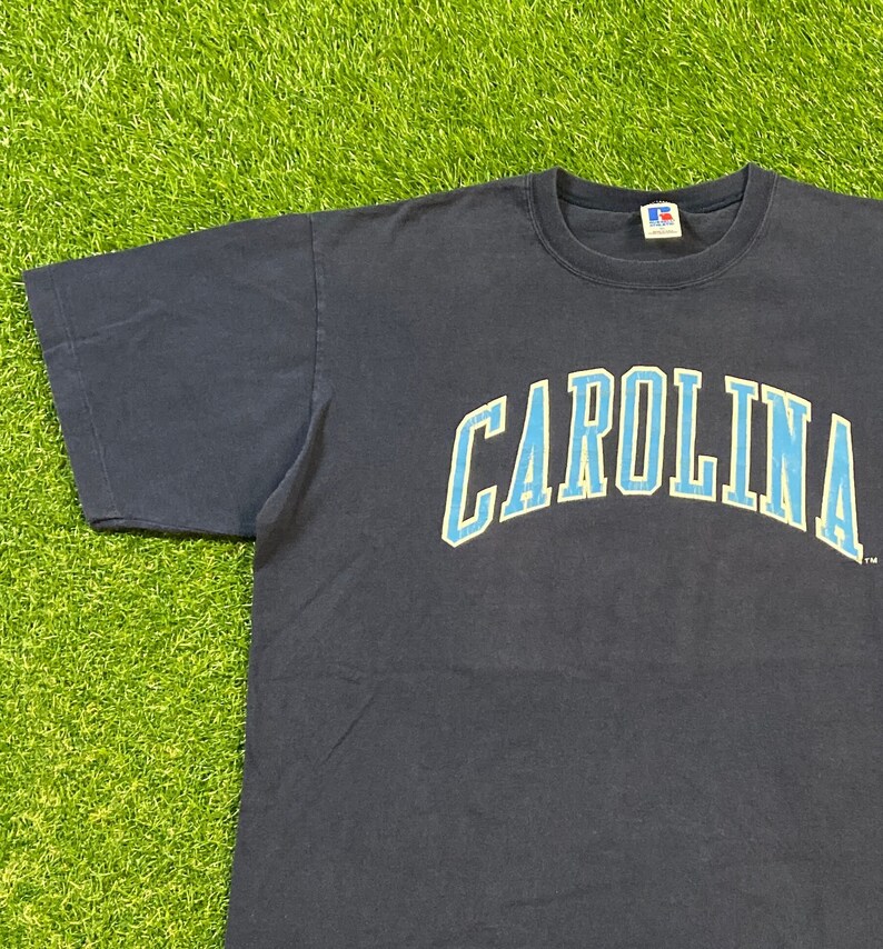 May include: A navy blue t-shirt with a light blue and white "CAROLINA" graphic on the front.