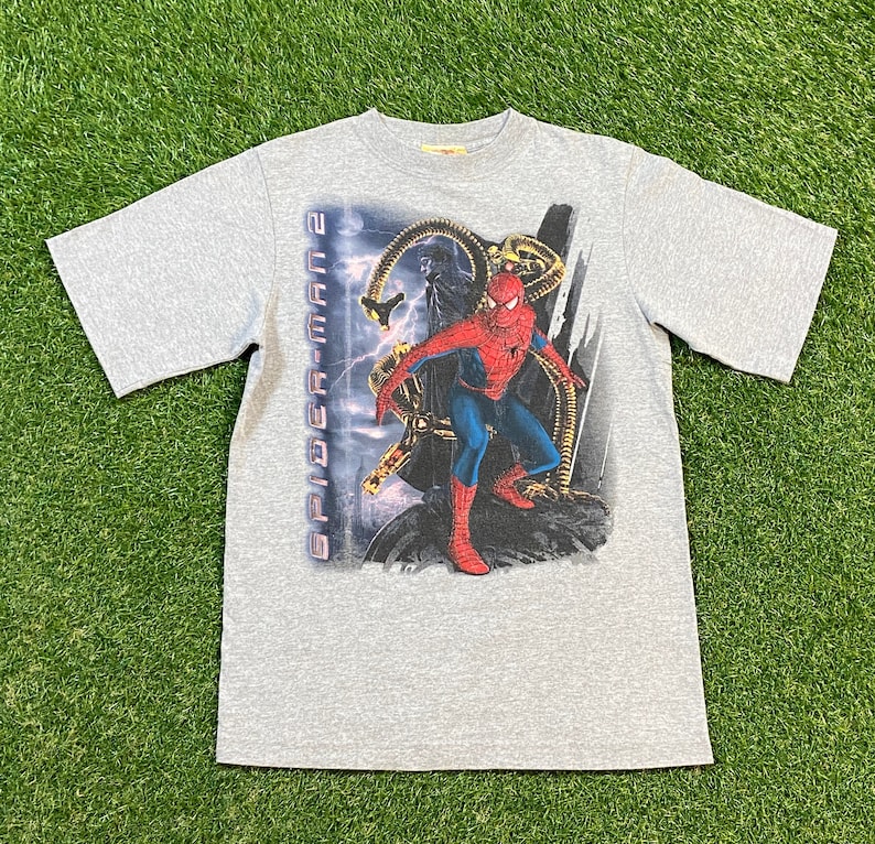 May include: A grey short-sleeved t-shirt with a graphic print of Spider-Man from the film Spider-Man 2. The graphic features Spider-Man fighting Doctor Octopus.