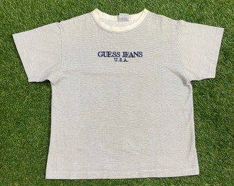 Könnte beinhalten: Weißes, gestreiftes T-Shirt mit einem blauen gestickten Logo, auf dem "GUESS JEANS U.S.A." steht.