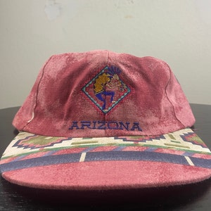 May include: A red and white baseball cap with a Native American design and the word "ARIZONA" embroidered on the front.