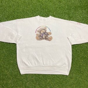 Könnte beinhalten: Weißer Langarm-Pullover mit einem Regenbogen-Motiv eines Teddybären und dem Text "Jesus loves me this much!"