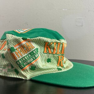 May include: Green and white baseball cap with the text "OFFICIAL DRINKER OF ST. PATRICK'S DAY" and "KILLIN' IT" in orange. The cap has a green bill.