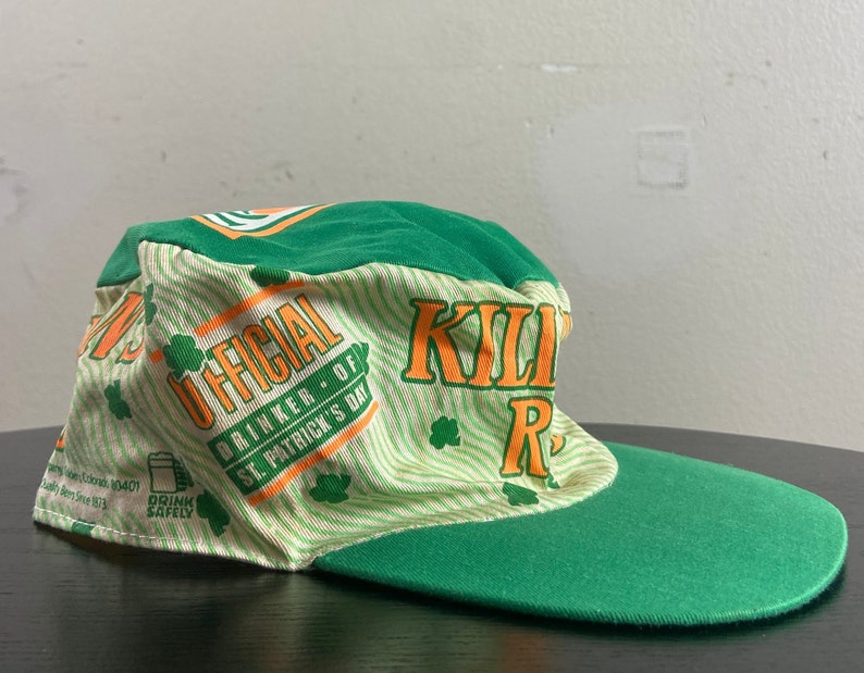 May include: Green and white baseball cap with the text "OFFICIAL DRINKER OF ST. PATRICK'S DAY" and "KILLIN' IT" in orange. The cap has a green bill.
