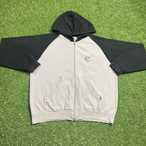 Puede incluir: Una sudadera gris con cremallera, mangas raglán negras y capucha negra. La sudadera tiene un bolsillo delantero a cada lado y un pequeño logotipo bordado en el pecho. La cremallera recorre el centro de la sudadera.