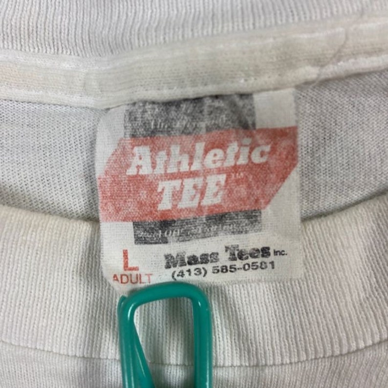 May include: White t-shirt with a red tag that says "Athletic TEE" and a smaller white tag that says "Mass Tees Inc. (413) 585-0501" and "Adult L".