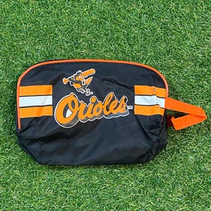 Könnte beinhalten: Schwarze und orangefarbene Baltimore Orioles Reisetasche mit Griff. Die Tasche zeigt das Teamlogo und das Wort "Orioles" in Orange und Weiß. Die Tasche hat orange und weiße Streifen.