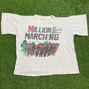 May include: White t-shirt with a black and red graphic print that says "Million People Marching". The graphic features a crowd of people marching with signs and flags.