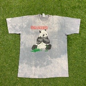 May include: A gray tie-dye t-shirt with a black and white giant panda illustration. The shirt has the word "ENDANGERED" printed in red above the panda and a description of the giant panda below the illustration.