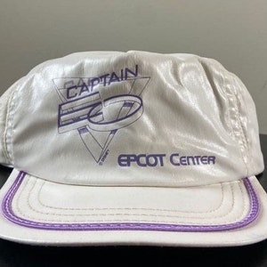 Puede incluir: Gorra de béisbol blanca con una visera morada y un logotipo morado que dice "Captain EO EPCOT Center".
