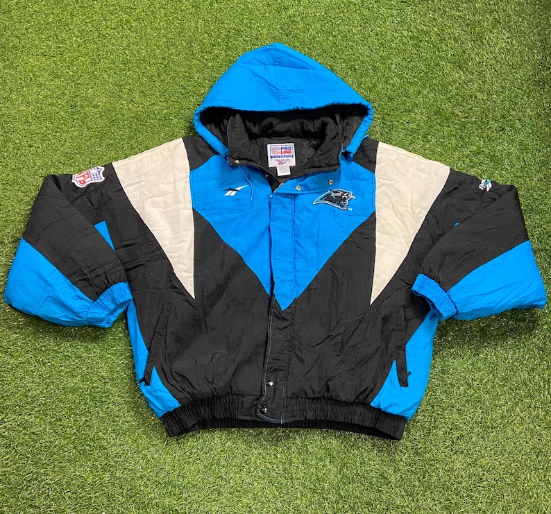Peut inclure: Veste &agrave; capuche bleue, noire et blanche avec le logo des Panthers de la Caroline. La veste a une base noire avec des accents bleus et blancs, une fermeture &eacute;clair compl&egrave;te et une capuche. La veste est fabriqu&eacute;e par Reebok.