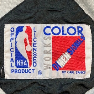 Może przedstawiać: Biała łatka z czarnymi szwami i tekstem "OFFICIAL NBA LICENSED PRODUCT" z logo koszyk&oacute;wki NBA i tekstem "COLOR WORKS DIMENSIONAL BY CARL BANKS".