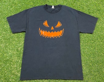 Peut inclure: Un t-shirt noir avec un motif de visage de citrouille orange.