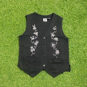 May include: Black sleeveless vest with a white embroidered design of cartoon characters. The vest has a button closure and two pockets.