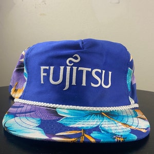 May include: A blue and white baseball cap with a floral print on the brim. The front of the cap has the word "FUJITSU" embroidered in white.